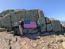 Pam and Hiram holding the flag below the first ascent plaque